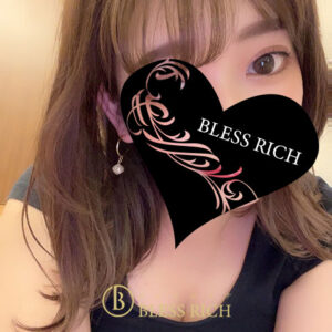 藤沢 メンズエステ｜完全個室 BLESS RICH（ブレスリッチ） Portrait of a woman with a black heart-shaped overlay covering the lower half of her face; the heart features pink floral designs and the words 'BLESS RICH'. A small gold logo and text reading 'BLESS RICH' appear near the neckline; an earring and her shoulder are visible.