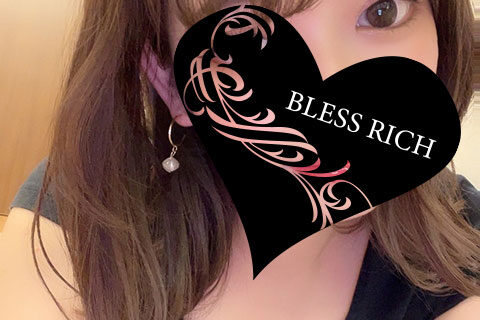 Portrait of a woman with a black heart-shaped overlay covering the lower half of her face; the heart features pink floral designs and the words 'BLESS RICH'. A small gold logo and text reading 'BLESS RICH' appear near the neckline; an earring and her shoulder are visible.